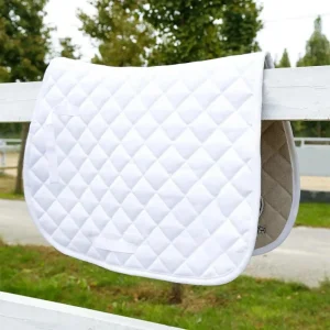 White quilted horse saddle pad hanging on a fence in a riding arena