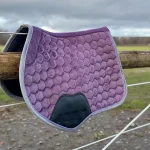 Purple hexagonal-patterned horse saddle pad hanging on a wooden fence.